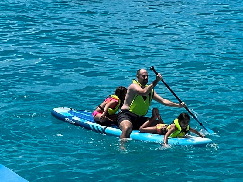 Father sitting on his paddleboard guiding two children alongside in Mullet Bay