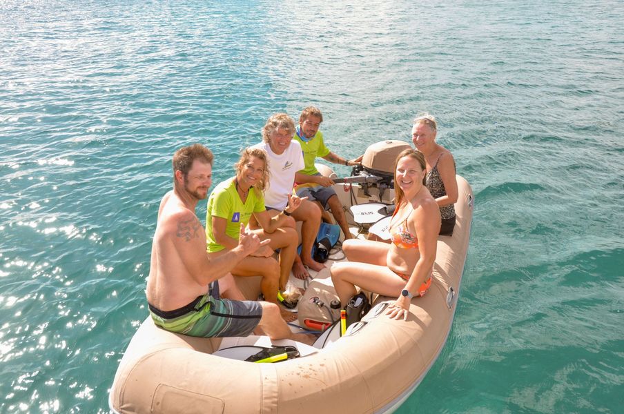 Three guests and two crew members smiling inside a small dinghy preparing to return to The Phoenix