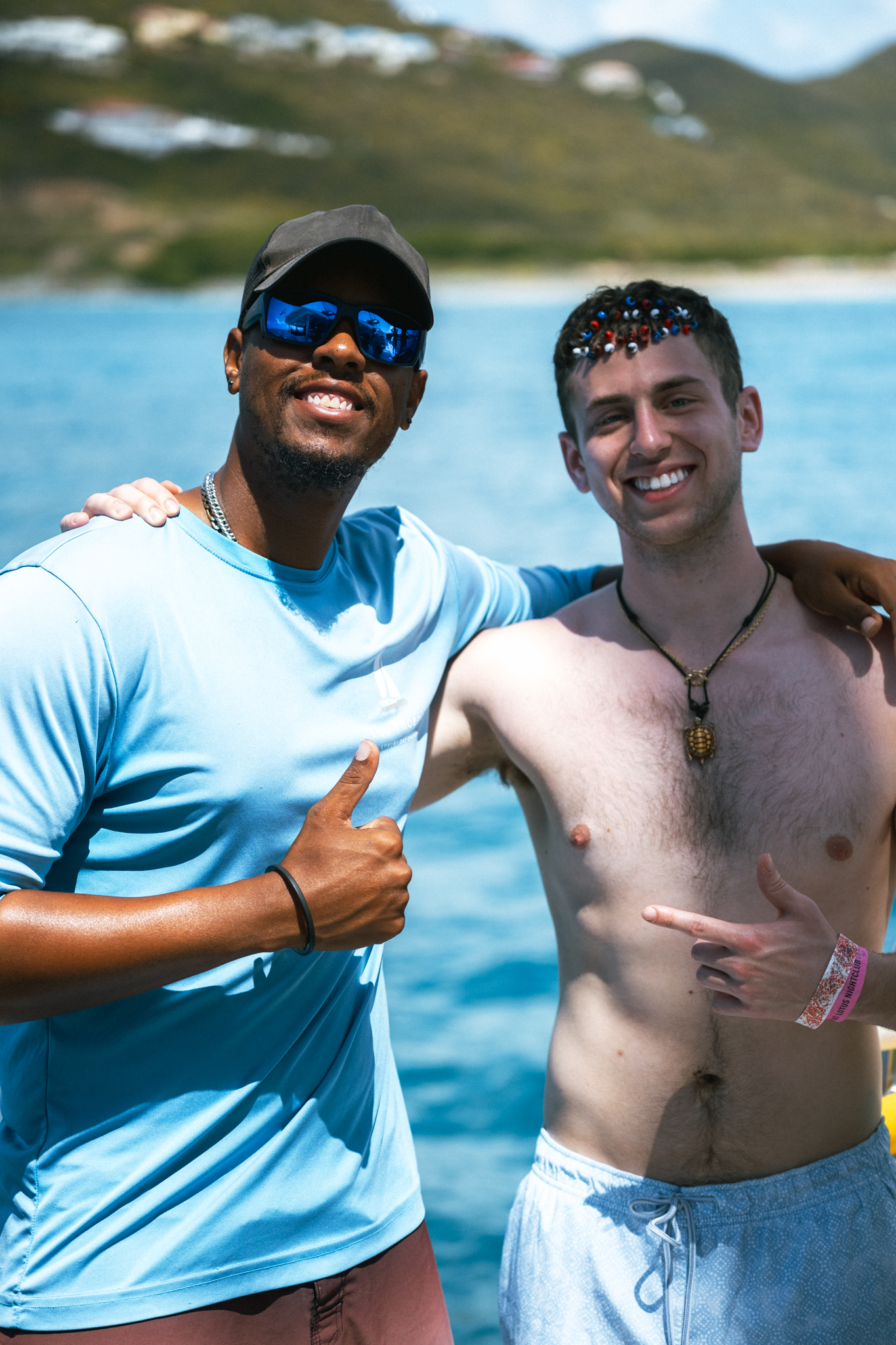 Crew member and guest smiling together on The Phoenix catamaran deck with St. Maarten hills behind